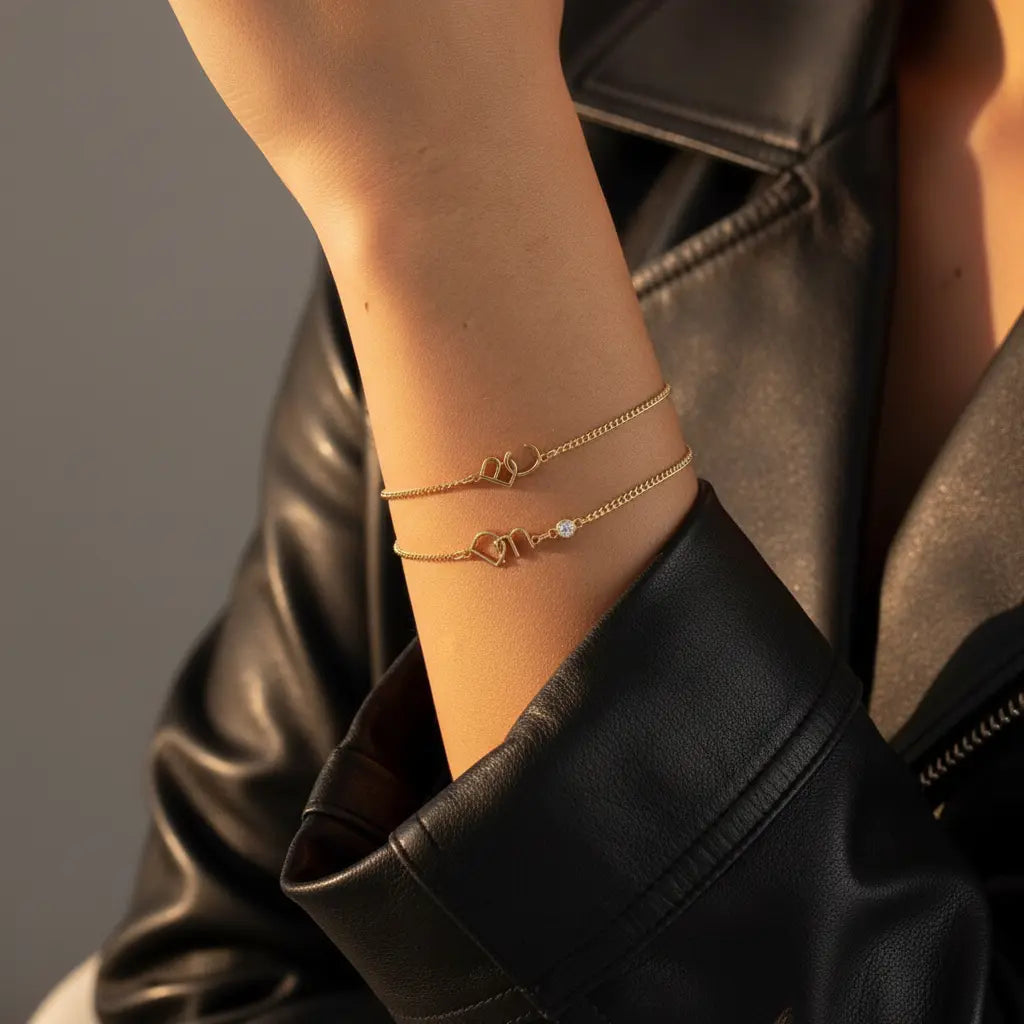 A close-up of a person's wrist wearing three delicate rose gold chain bracelets, styled with a black leather jacket.